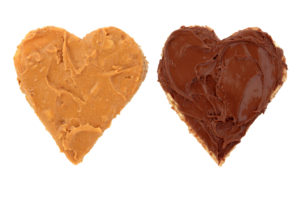 Peanut butter and chocolate spread on heart shaped bread isolated over white background.
