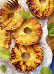 Grilled pineapple slices with addition of honey on a blue table, top view
