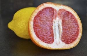 A grapefruit and a lemon are on dark brown background.