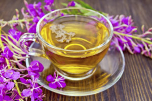 Herbal tea in a glass cup and fresh flowers fireweed against the backdrop of wooden planks